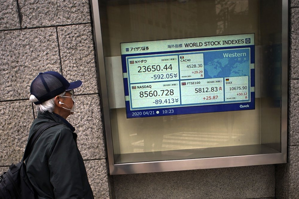 A man wearing a mask against the spread of the new coronavirus looks at an electronic stock board showing world stock indexes at a securities firm in Tokyo Tuesday, April 21, 2020.