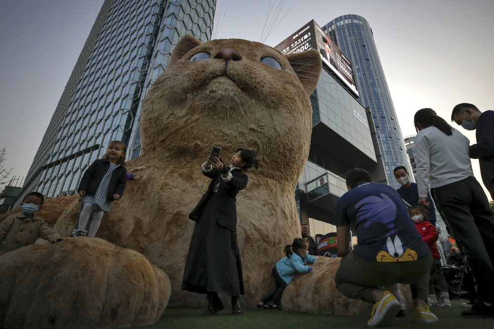 A woman takes a selfie as visitors wearing face masks to help curb the spread of the coronavirus gather near a giant cat structure on display at a commercial office building in Beijing, Sunday, Oct. 18, 2020.