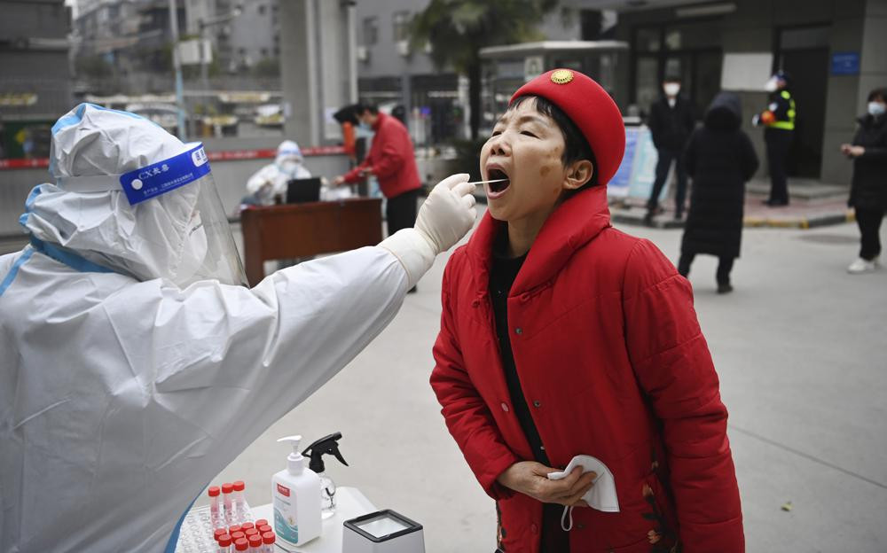 In this photo released by China's Xinhua News Agency, a worker wearing protective gear gives a COVID-19 test to a woman at a testing site in Xi'an in northwestern China's Shaanxi Province, Tuesday, Jan. 4, 2022.