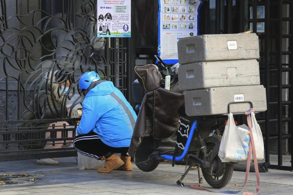 A delivery worker passes groceries to a masked woman through a closed gate at a residential block in Xi'an, a city of 13 million people under the COVID-19 lockdown, in northwest China's Shaanxi province on Monday, Jan. 10, 2022.