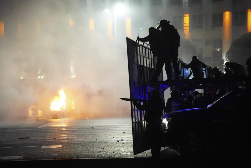 A police car on fire as riot police prepare to stop protesters in the center of Almaty, Kazakhstan, on Jan. 5, 2022.