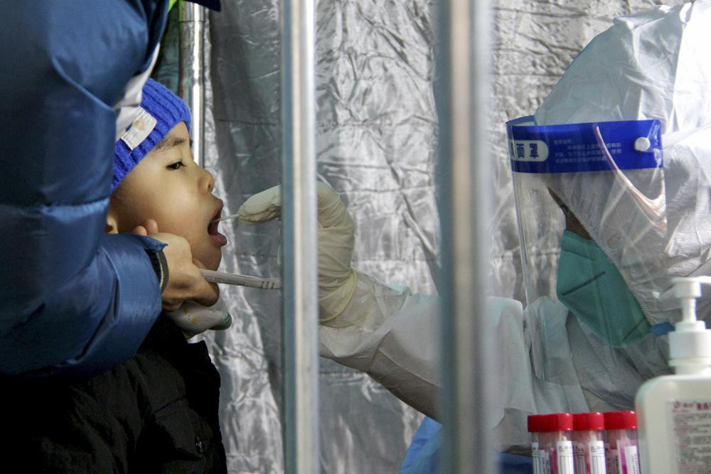 In this photo released by Xinhua News Agency, a child gets a throat swab for the COVID-19 test at a residential area in Fengtai District in Beijing, Sunday, Jan. 23, 2022.