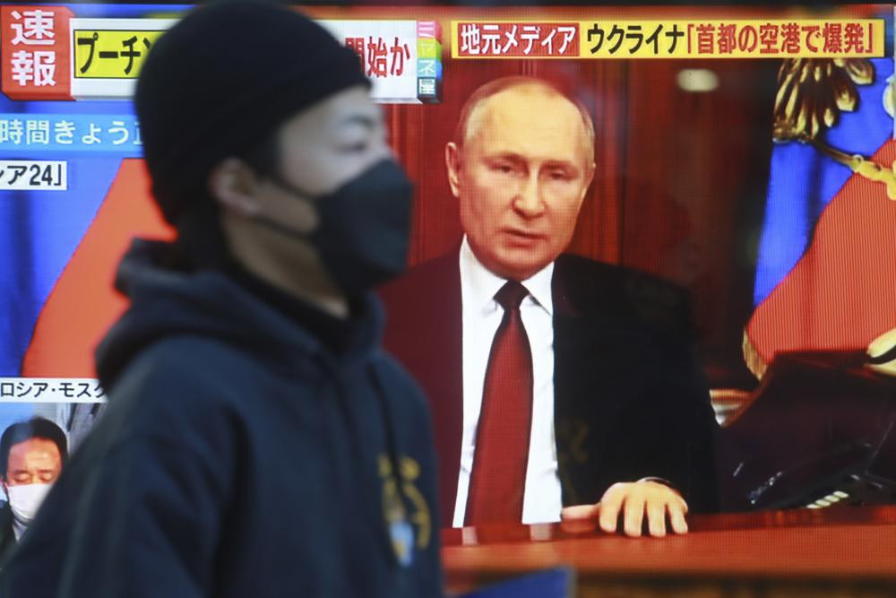 A man walks past a TV screen with image of Russia's President Vladimir Putin in Tokyo, Thursday, Feb. 24, 2022.