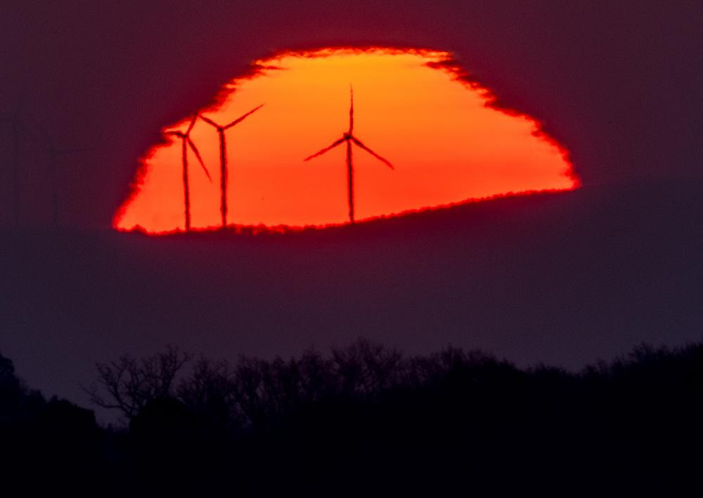 Wind turbines stand in front of the rising sun in Frankfurt, Germany, Friday, March 11, 2022.