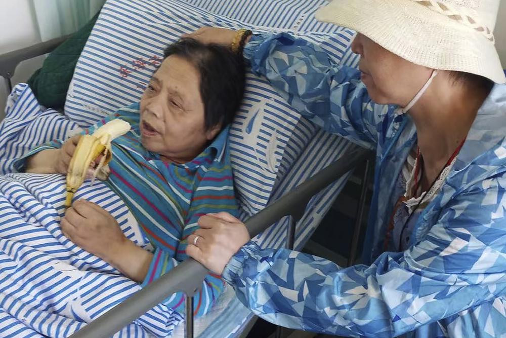In this photo released by the family of Shen Peiming, Shen Peiming, 71, eats a banana as a family member attends to her at her bed side at the Shanghai Donghai Elderly Care hospital on Sept. 24, 2019.