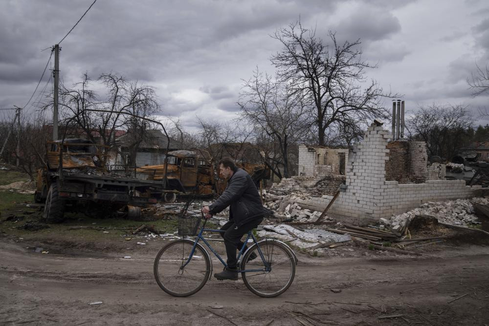 A man rides a bicycle past destroyed vehicles and an apartment building in Yahidne, near of Dnipro, Ukraine, Tuesday, April 12, 2022.