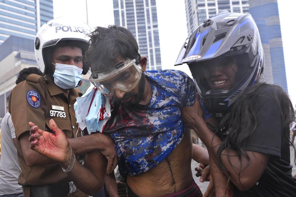 A Sri Lankan policeman, left, and a civilian helps an anti-government protester who was beaten up by government supporters during a clash in Colombo, Sri Lanka, Monday, May 9, 2022.