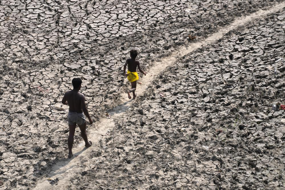 A man and a boy walk across the almost dried up bed of river Yamuna following hot weather in New Delhi, India, Monday, May 2, 2022.