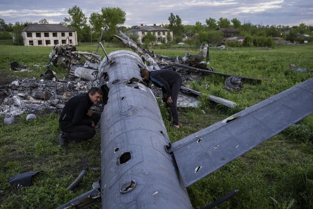 Oleksiy Polyakov, right, and Roman Voitko check the remains of a destroyed Russian helicopter lie in a field in the village of Malaya Rohan, Kharkiv region, Ukraine, Monday, May 16, 2022.