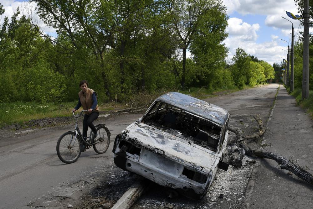 A man rides a bicycle past a car destroyed by shelling in a street in the village of Niu-York, Donetsk region, Ukraine, Monday, May 16, 2022.