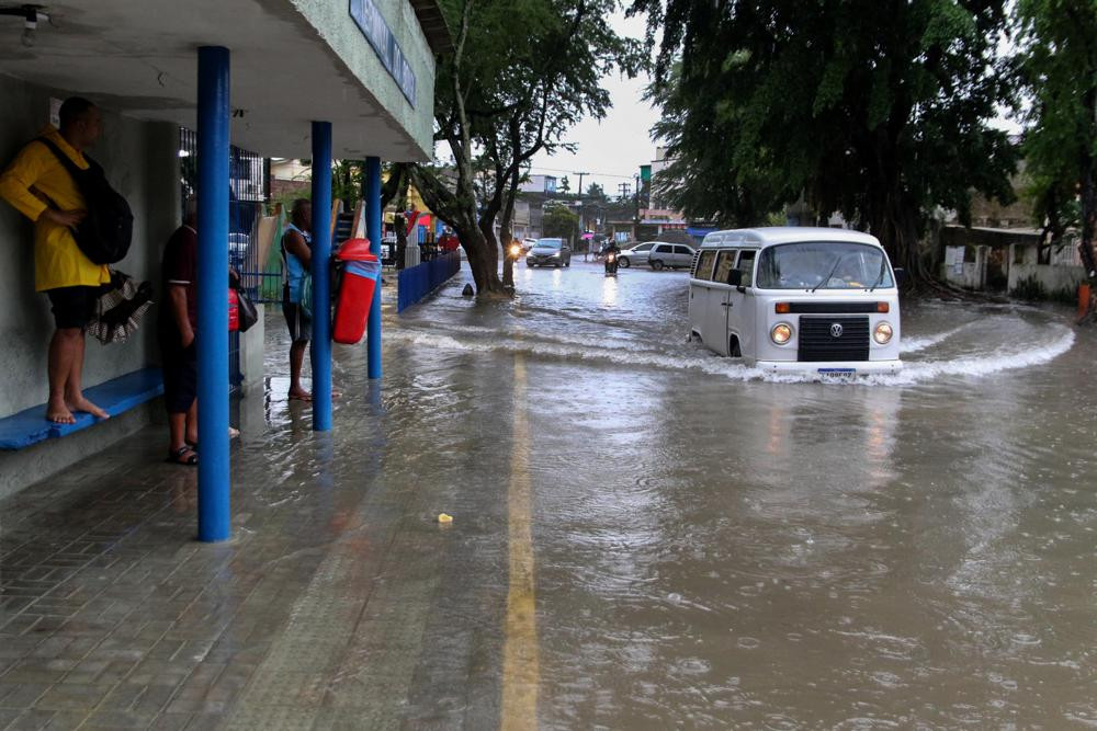 A woman stands on a bus stop bench as a driver of a Volkswagen van navigates a flooded street in Recife, state of Pernambuco, Brazil, Saturday, May 28, 2022.