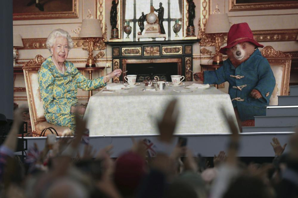 The crowd watch a film of Queen Elizabeth II having tea with Paddington Bear on a big screen at the Platinum Jubilee concert taking place in front of Buckingham Palace, London, Saturday June 4, 2022.