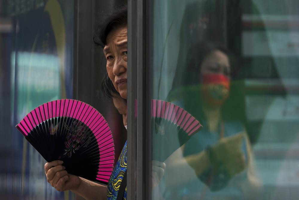 A woman fans herself at an advertisement boards on a bus stand reflecting a masked commuter as they wait for buses in Beijing, Tuesday, July 5, 2022. AP/RSS Photo