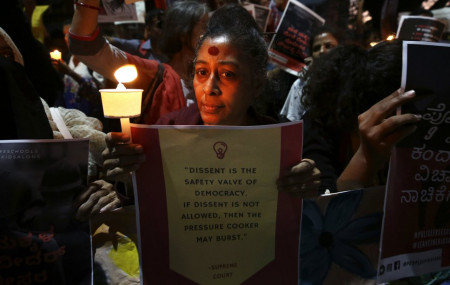In this Tuesday, Feb. 4, 2020 photo, an Indian woman holds a candle and placard during a protest against the sedition case filed by police against a school after a play preformed by students denouncing a new citizenship law, in Bangalore, India.
