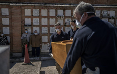 The daughter and husband, center left, no names available, of an elderly victim of the COVID-19 stand as undertakers place the coffin in the grave at the Almudena cemetery in Madrid, Spain, Saturday March 28, 2020.