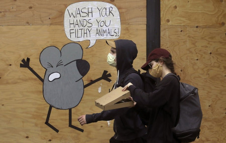 - In this May 2, 2020, file photo, a man and woman wearing masks to prevent the spread of the coronavirus walk past a cartoon advising people to wash their hands on a boarded up storefront in San Francisco.