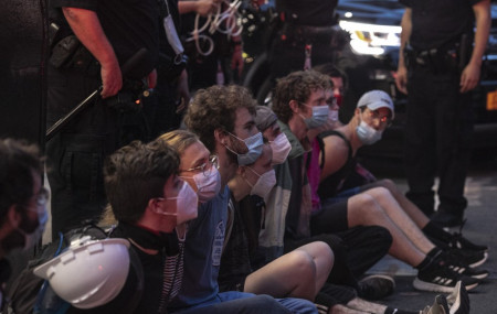 Protesters who were arrested by police for breaking a curfew during a solidarity rally calling for justice over the death of George Floyd, sit on a sidewalk as they wait to be taken away in a van on Thursday, June 4, 2020, in New York.