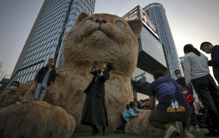 A woman takes a selfie as visitors wearing face masks to help curb the spread of the coronavirus gather near a giant cat structure on display at a commercial office building in Beijing, Sunday, Oct. 18, 2020.