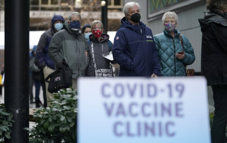 In this an. 24, 2021, file photo, people stand near a sign as they wait in line to receive the first of two doses of the Pfizer vaccine for COVID-19 at a one-day vaccination clinic set up in an Amazon.com facility in Seattle.