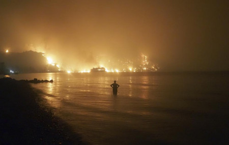 In this file photo dated Friday, Aug. 6, 2021, a man watches as wildfires approach Kochyli beach near Limni village on the island of Evia, about 160 kilometers (100 miles) north of Athens, Greece.