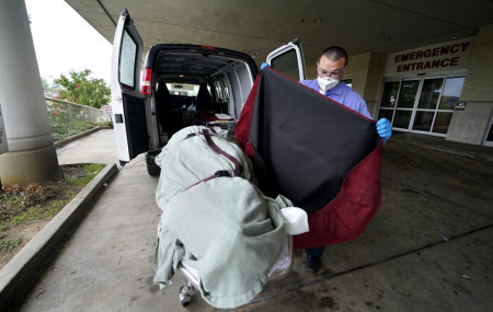 In this Aug. 18, 2021, file photo, an employee of a local funeral home covers the body of a COVID-19 patient who died as he prepares to take it away from a loading dock, at the Willis-Knighton Medical Center in Shreveport, Louisiana.
