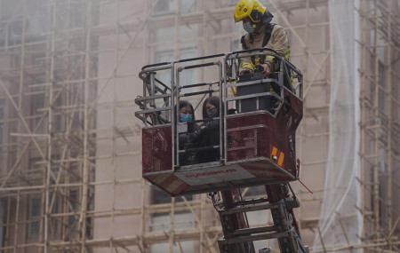 Two women are rescued by a firefighter in a bucket crane outside the World Trade Centre located in the city's popular Causeway Bay shopping district of Hong Kong, Wednesday, Dec. 15, 2021.