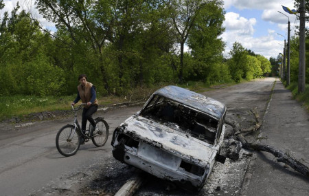 A man rides a bicycle past a car destroyed by shelling in a street in the village of Niu-York, Donetsk region, Ukraine, Monday, May 16, 2022.