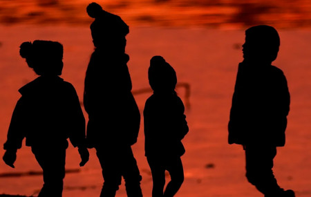Kids are silhouetted against a pond at a park in Lenexa, Kansas, on Saturday, Dec. 26, 2020.