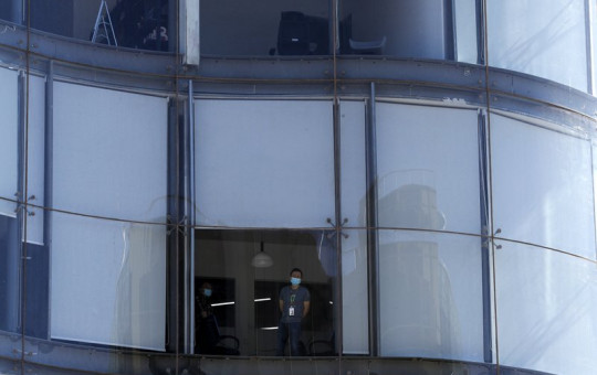 A masked worker looks out from his office in Beijing, Tuesday, March 10, 2020.