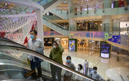 In this April 15, 2020 photo, people wear facemasks to protect against the spread of the new coronavirus cleans as they ride an escalator at a shopping mall in Beijing.