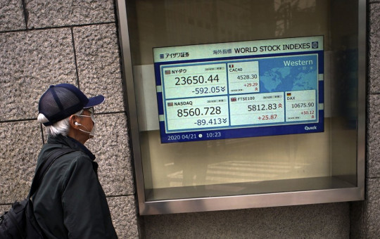 A man wearing a mask against the spread of the new coronavirus looks at an electronic stock board showing world stock indexes at a securities firm in Tokyo Tuesday, April 21, 2020.