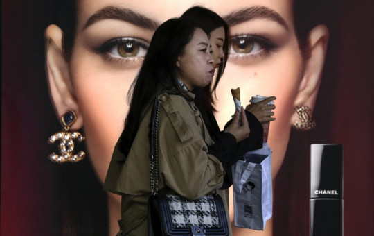 In this Oct. 19, 2020, file photo, women eating snack walk by a Chanel cosmetic shop at the capital city's popular shopping mall in Beijing.