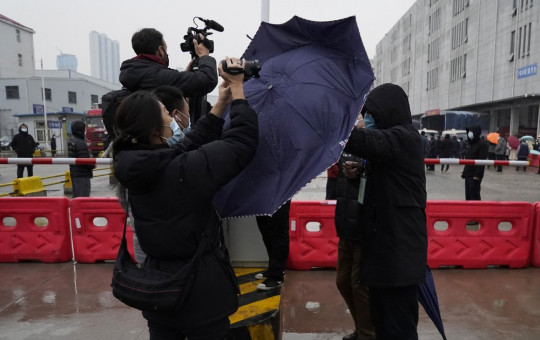 A plainclothes security person uses his umbrella to block journalists from filming after the WHO team arrives at the Baishazhou wholesale market on the third day of field visit in Wuhan in central China's Hubei province on Sunday, Jan. 31, 2021.