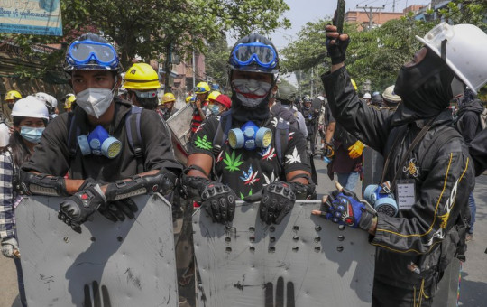 In this March 9, 2021, file photo, anti-coup protesters with makeshift shields take positions while one man looks at his phone in Mandalay, Myanmar.