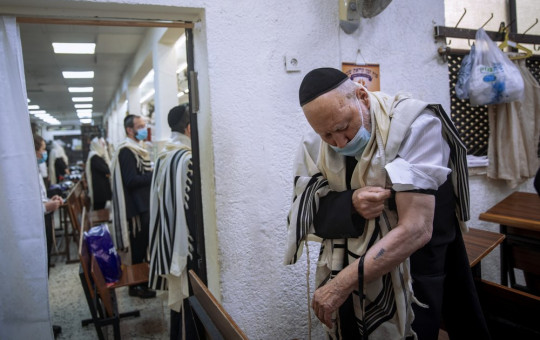 Holocaust survivor Yehoshua Datsinger places tefillin on his arm above the Auschwitz concentration camp identification number tattoo, during morning prayer at a synagogue limited to 20 people during lockdown, in Bnei Brak, Israel, Monday.