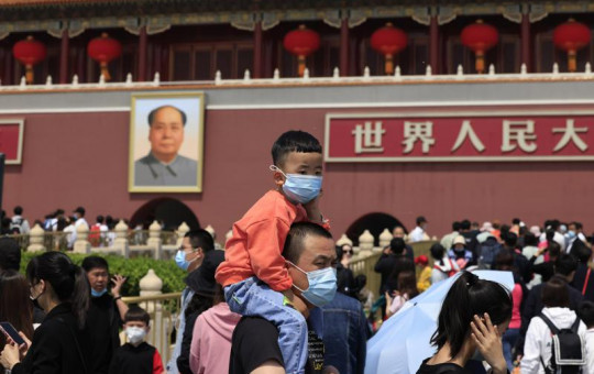 In this May 3, 2021, file photo, a man and child wearing masks visit Tiananmen Gate near the portrait of Mao Zedong in Beijing.