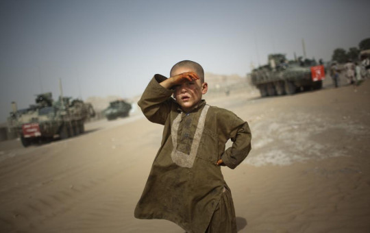 In this Aug. 6, 2009 file photo, a child watches military vehicles of 5th Striker Brigades drive past his village on the outskirts of Spin Boldak, about 100 kilometers (63 miles) southeast of Kandahar, Afghanistan.