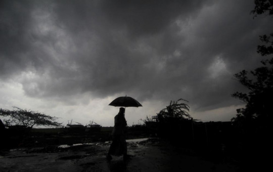 A villager holds an umbrella as dark clouds loom over Balasore district in Odisha, India, Tuesday, May 25, 2021, ahead of a powerful storm barreling toward the eastern coast.