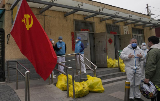 Community workers outside a locked down community chat near a Communist Party flag and trash bags labelled as hazardous waste on Thursday, March 17, 2022, in Beijing.