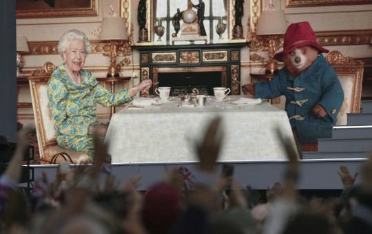 The crowd watch a film of Queen Elizabeth II having tea with Paddington Bear on a big screen at the Platinum Jubilee concert taking place in front of Buckingham Palace, London, Saturday June 4, 2022.