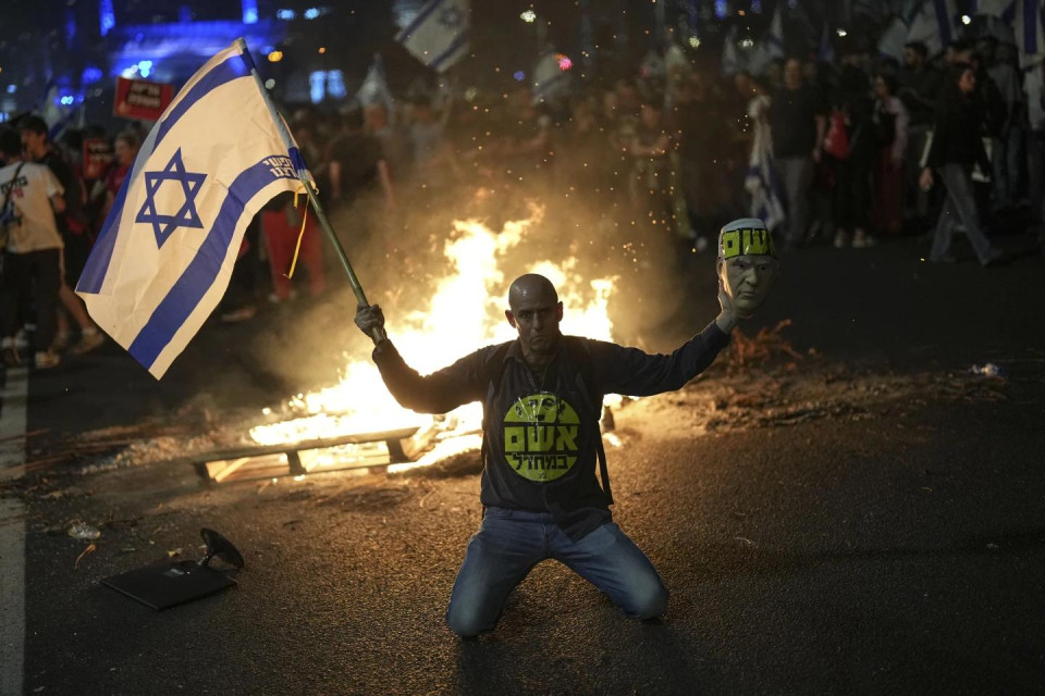 A protester holds an Israeli flag as Israelis light a bonfire during a protest after Prime Minister Benjamin Netanyahu has dismissed his defense minister Yoav Gallant in a surprise announcement in Tel Aviv, Israel, Tuesday, Nov. 5, 2024. (AP Photo)