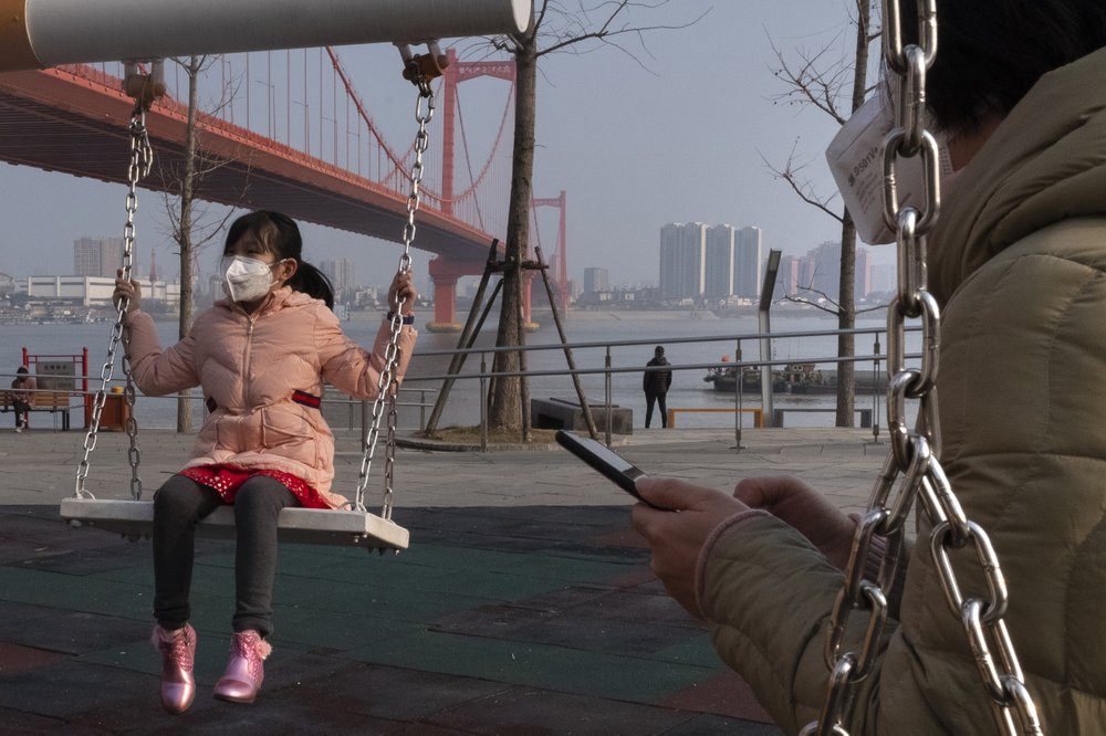 A girl wears a face mask as she play on a swing near the Yingwuzhou Yangtze River Bridge in Wuhan in central China's Hubei Province, Wednesday, Jan. 29, 2020.