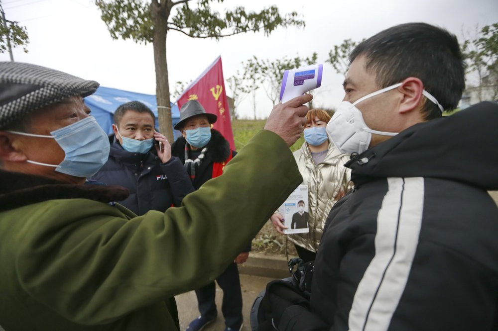 In this Saturday, Feb. 1, 2020, photo, a government worker takes the temperature of a passer-by at a checkpoint in Suining in southwestern China's Sichuan Province.