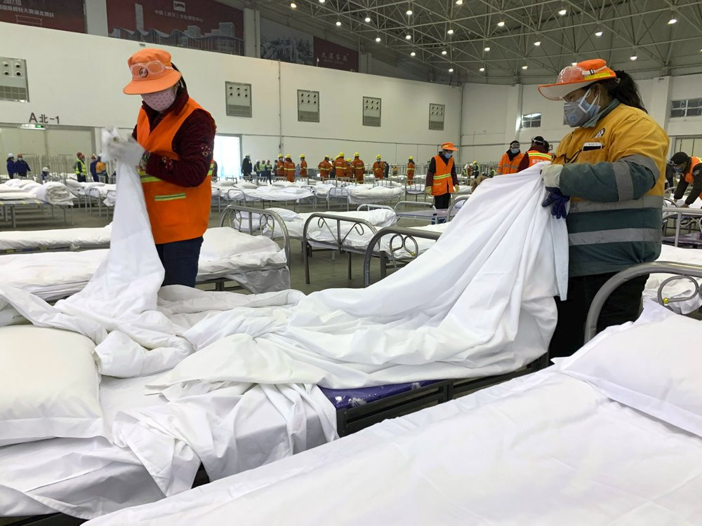 Workers arrange beds in a convention center that has been converted into a temporary hospital in Wuhan in central China's Hubei Province, Tuesday, Feb. 4, 2020.