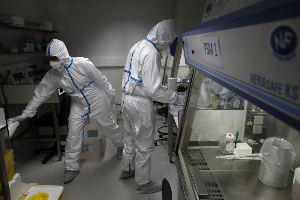 French lab scientists in hazmat gear inserting liquid in test tube manipulate potentially infected patient samples at Pasteur Institute in Paris, Thursday, Feb. 6, 2020.