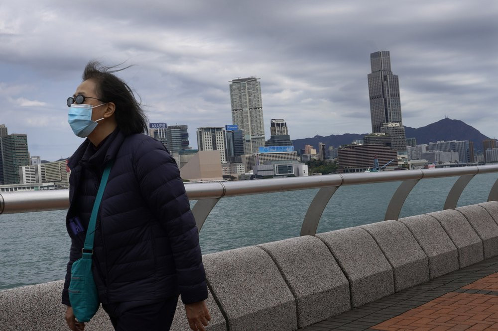 A woman wearing a face mask walks at the waterfront against the Victoria Habour in Hong Kong Sunday, Feb. 16, 2020. COVID-19 viral illness has sickened tens of thousands of people in China si