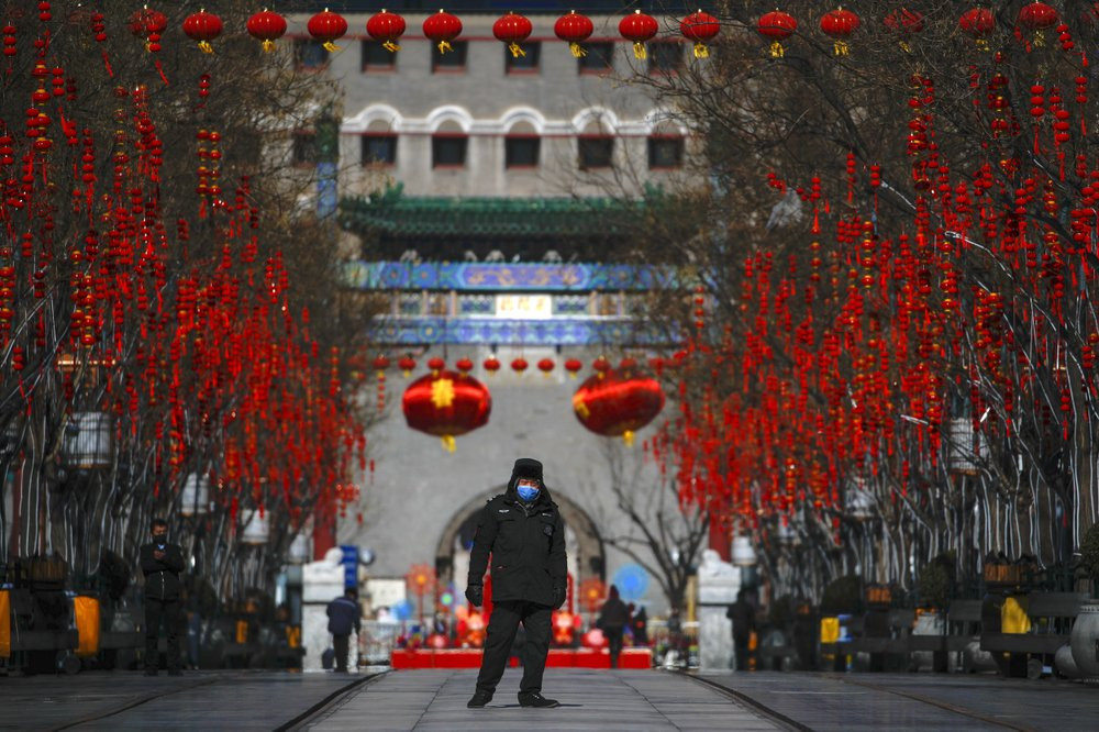 A security guard wearing a face mask walks through a quiet main Qianmen Street, a popular tourist spot, in Beijing, Sunday, Feb. 16, 2020.