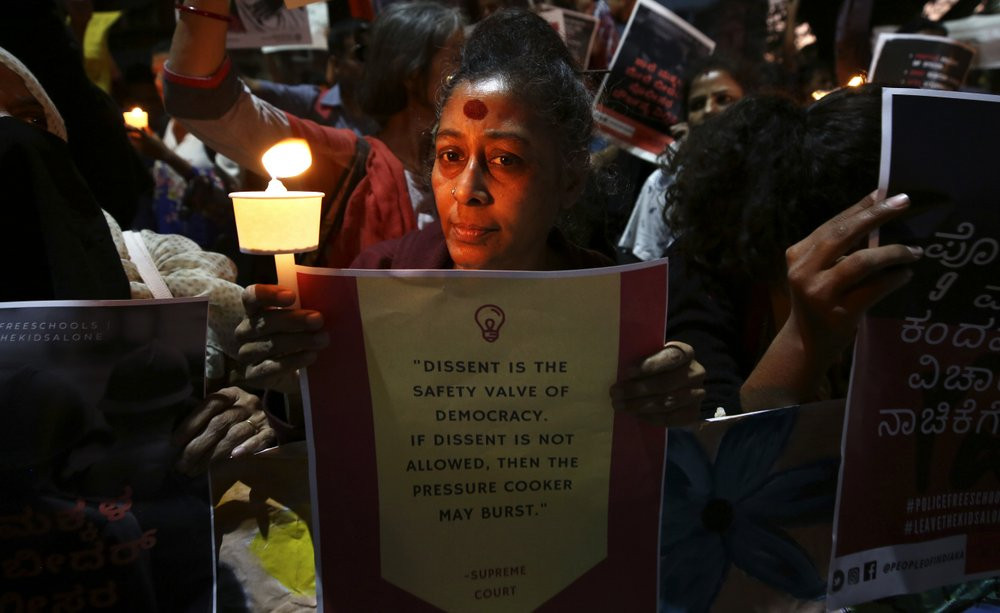 In this Tuesday, Feb. 4, 2020 photo, an Indian woman holds a candle and placard during a protest against the sedition case filed by police against a school after a play preformed by students 