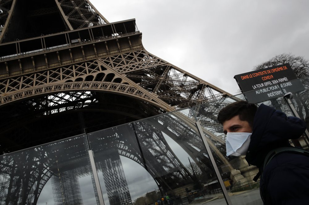 A man wearing a mask walks pasts the Eiffel tower closed after the French government banned all gatherings of over 100 people to limit the spread of the virus COVID-19, in Paris, Saturday, Ma