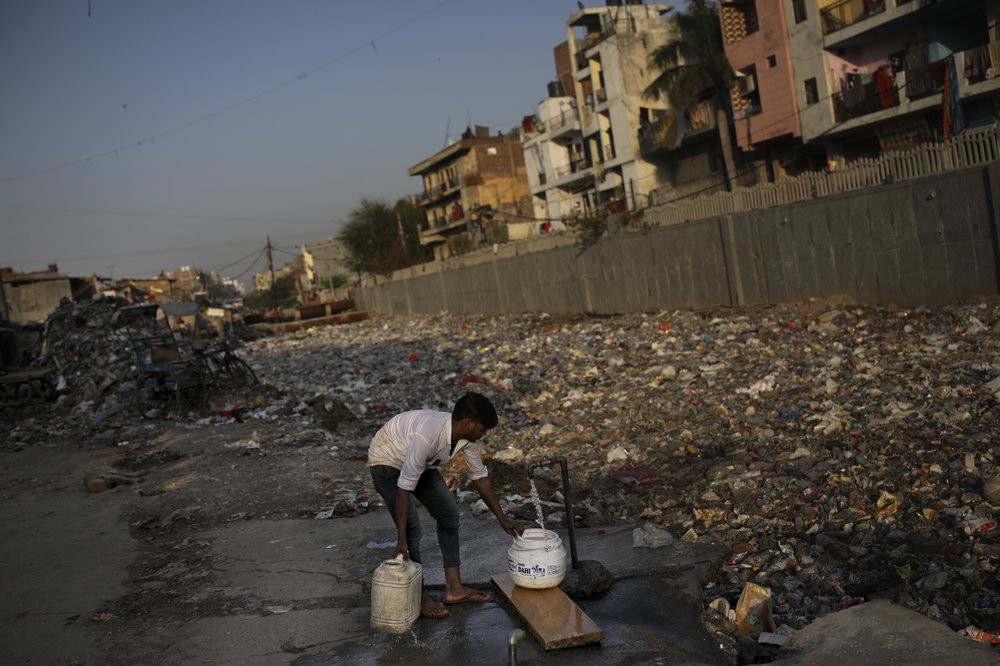 In this Tuesday, March 17, 2020 photo, a slum dweller fills water from a tap next to a drain filled with plastic and other filth in New Delhi, India.